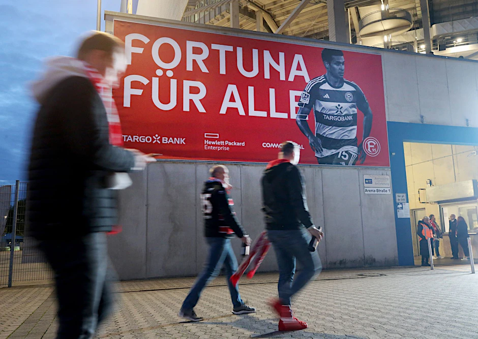 ARCHIV - Zuschauer gehen im Stadion an einem Transparent mit der Aufschrift "Fortuna für alle" vorbei.  