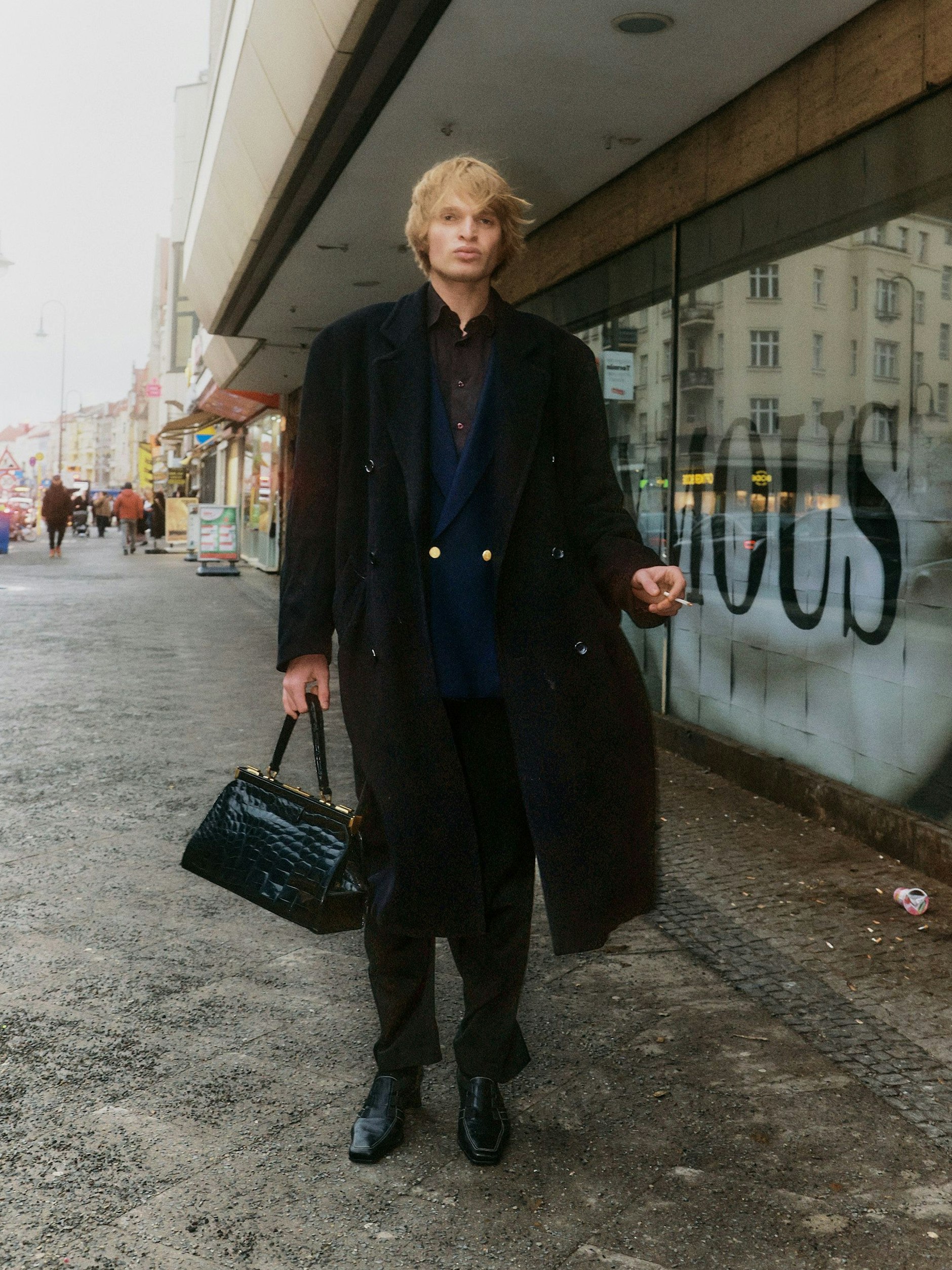 Das Outfit von Alexander ist spektakulär. Zentrales Piece ist ein Blazer von Yves Saint Laurent. Dazu kombiniert er einen Oversized-Mantel, Anzughose, hochhackige Schuhe und eine Handtasche mit Klippverschluss.