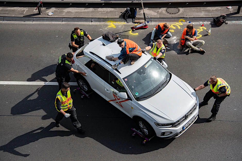 Kurioses Bild: Polizisten müssen ein Auto auf den Standstreifen der A100 in Berlin schieben. Zuvor hatten Aktivisten der Klimagruppe "Letzte Generation" die Straße blockiert.&nbsp;