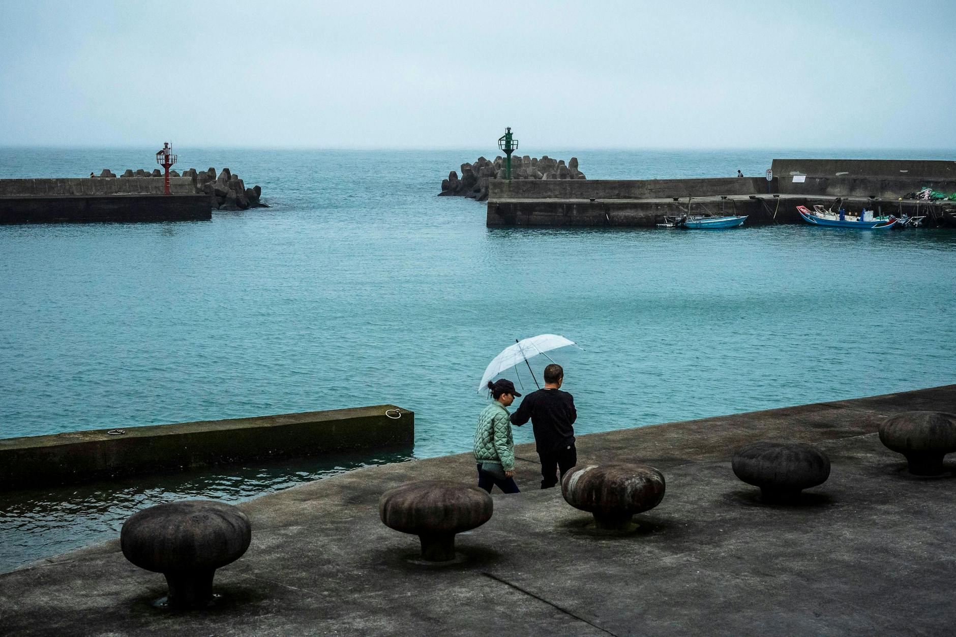 Ein Paar mit einem Regenschirm spaziert entlang des Fischerhafens an der Küste des Ostchinesischen Meeres im Bezirk Sanzhi in der Nähe von Taipeh, Taiwan.