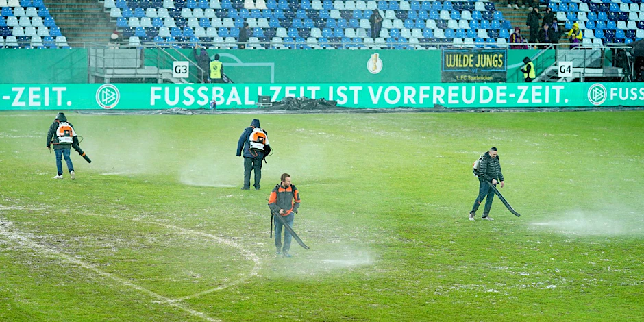 Arbeiter versuchten, Wasserlachen vom Spielfeld im Ludwigsparkstadion zu entfernen.  