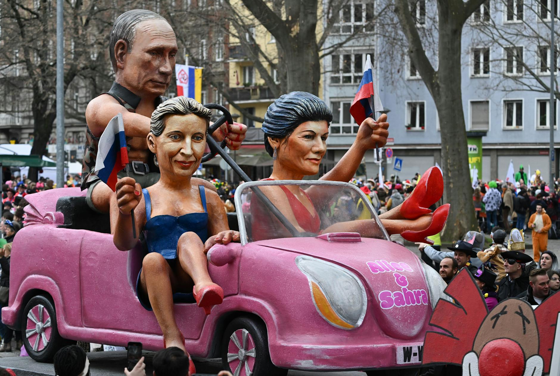 Beim Mainzer Carneval sitzen Alice Weidel (AfD) und Sahra Wagenknecht (BSW) in legeren Kleidchen in einem Auto, das von Russlands Präsident Wladimir Putin gesteuert wird. Dabei schwenken die beiden Damen Russlandfähnchen.