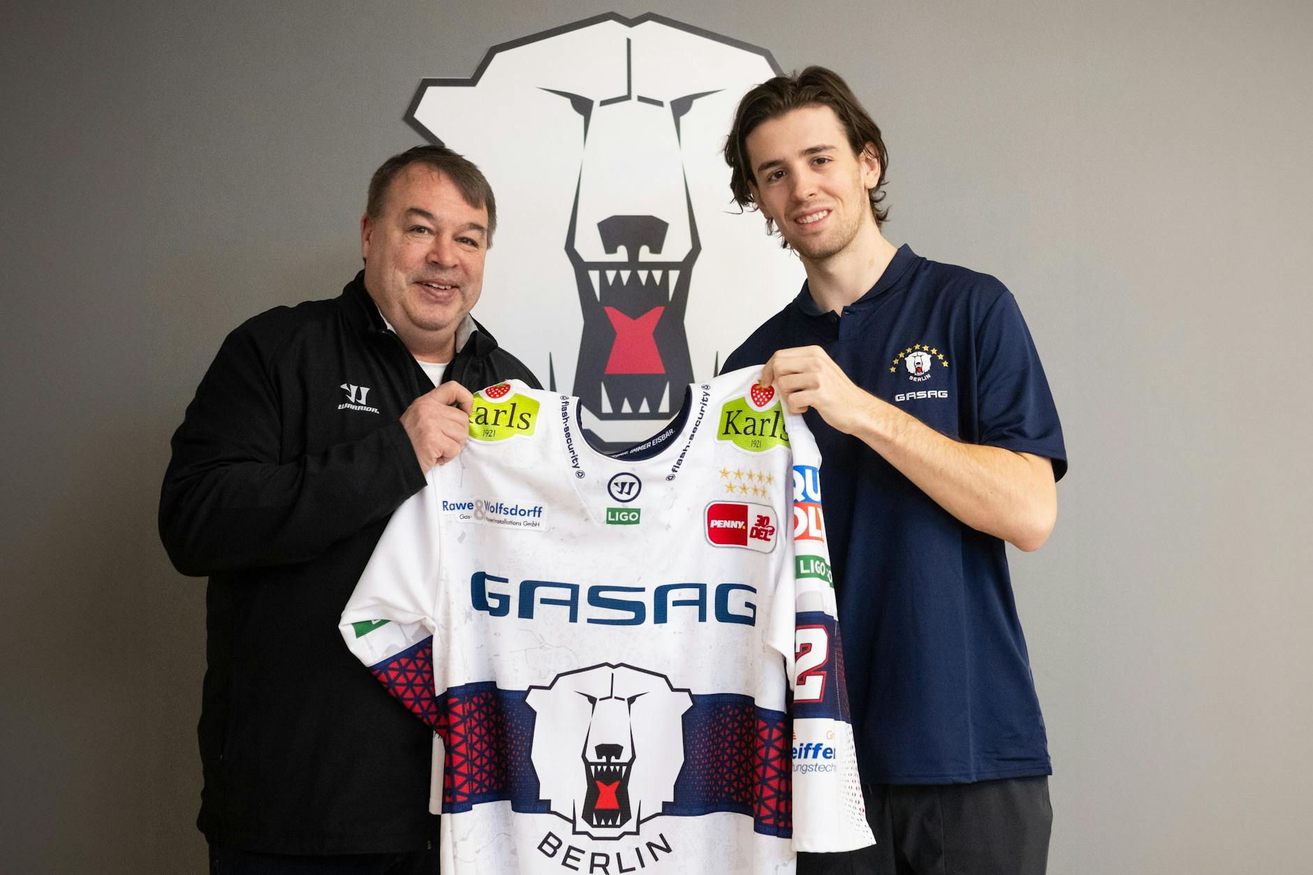 Eisbären-Sportdirektor Stephane Richer und Neuzugang Thomas Schemitsch halten das Trikot unterm Eisbären-Logo.