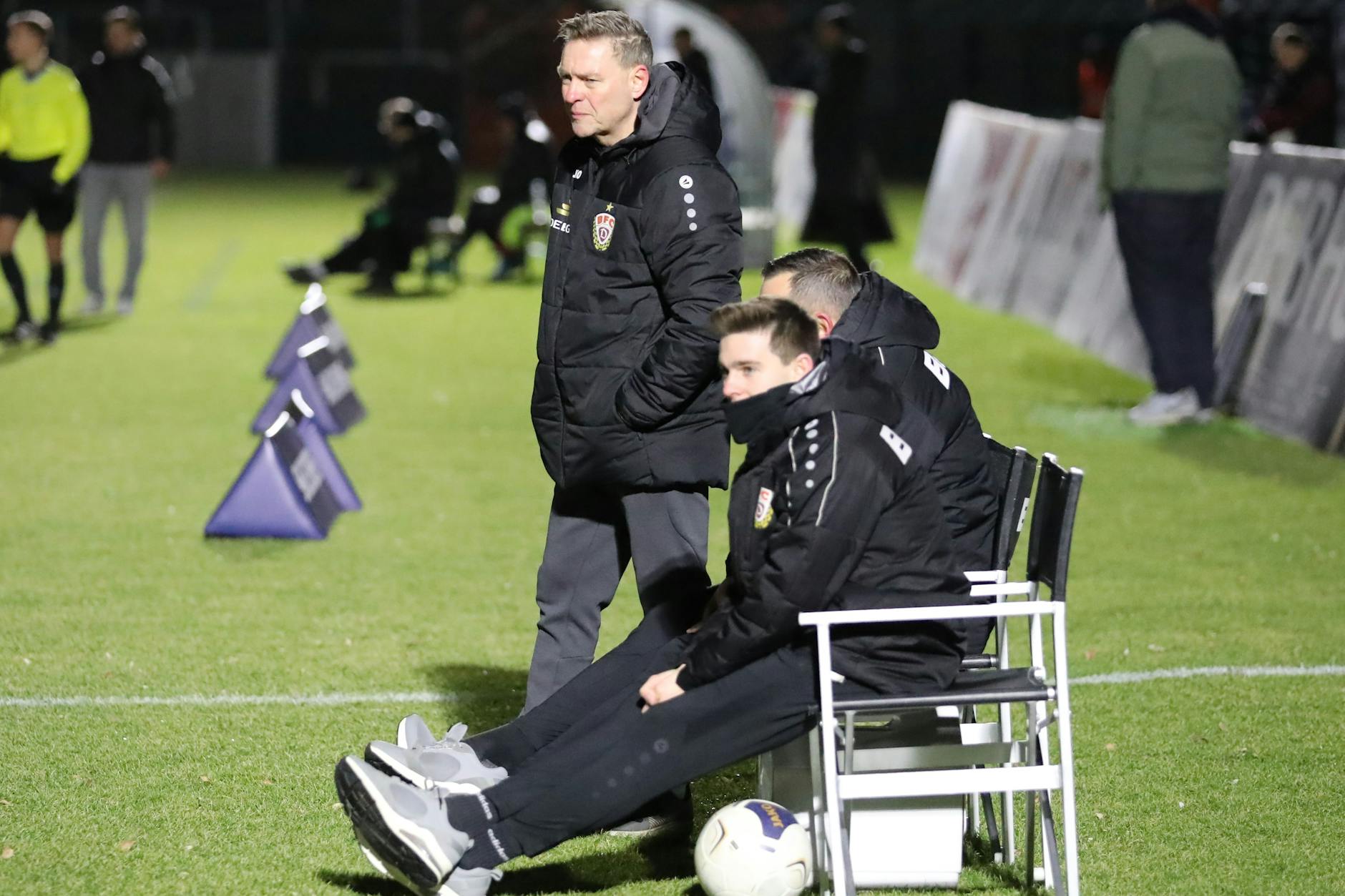 Dirk Kunert steht an der Bank, darauf sitzen Torwart-Trainer Carsten Nulle und Co-Trainer Nils Weiler (r.).