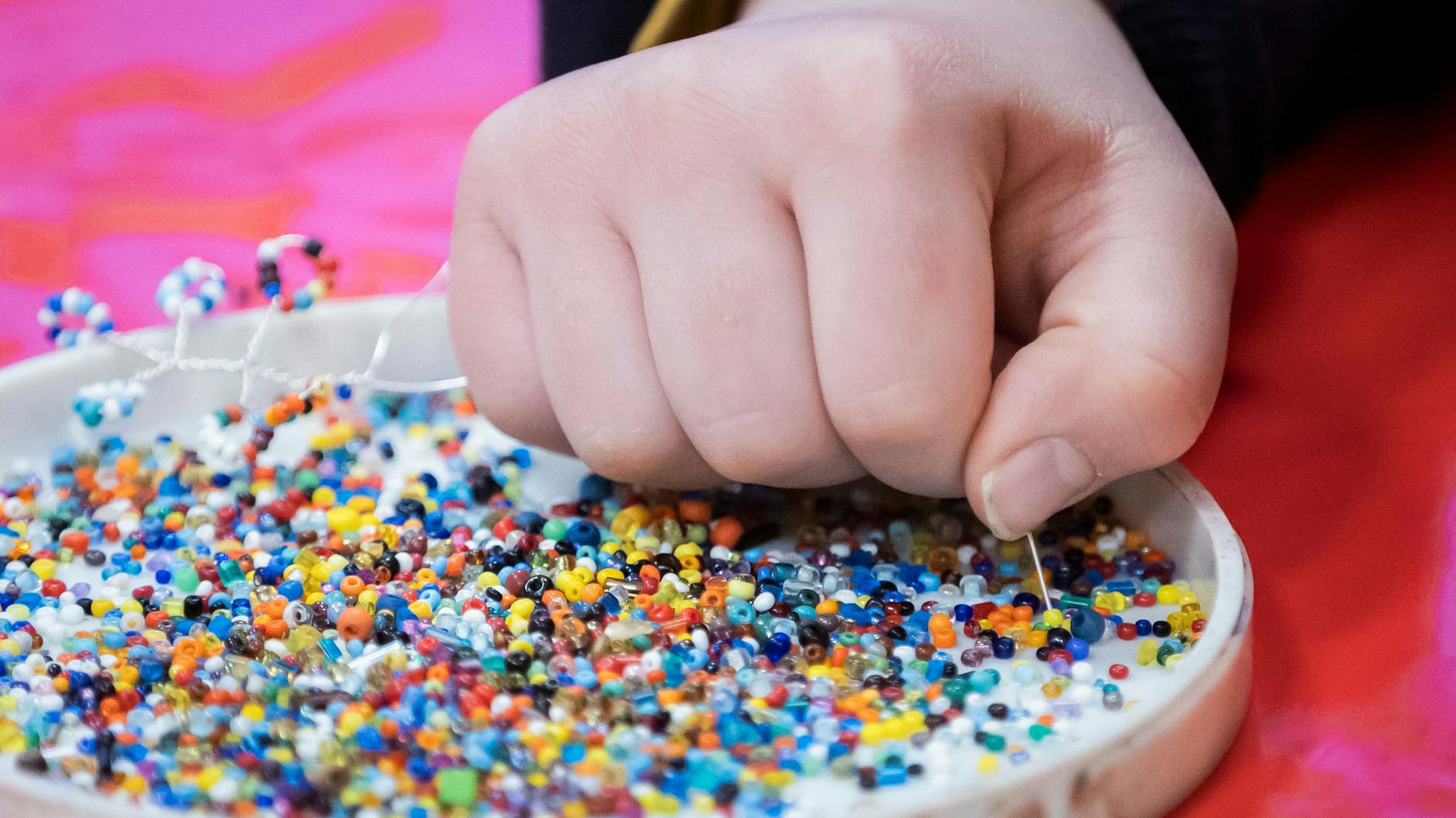 Ein Mädchen fädelt im Kinderklubhaus Perlen für ein Perlenbäumchen auf.