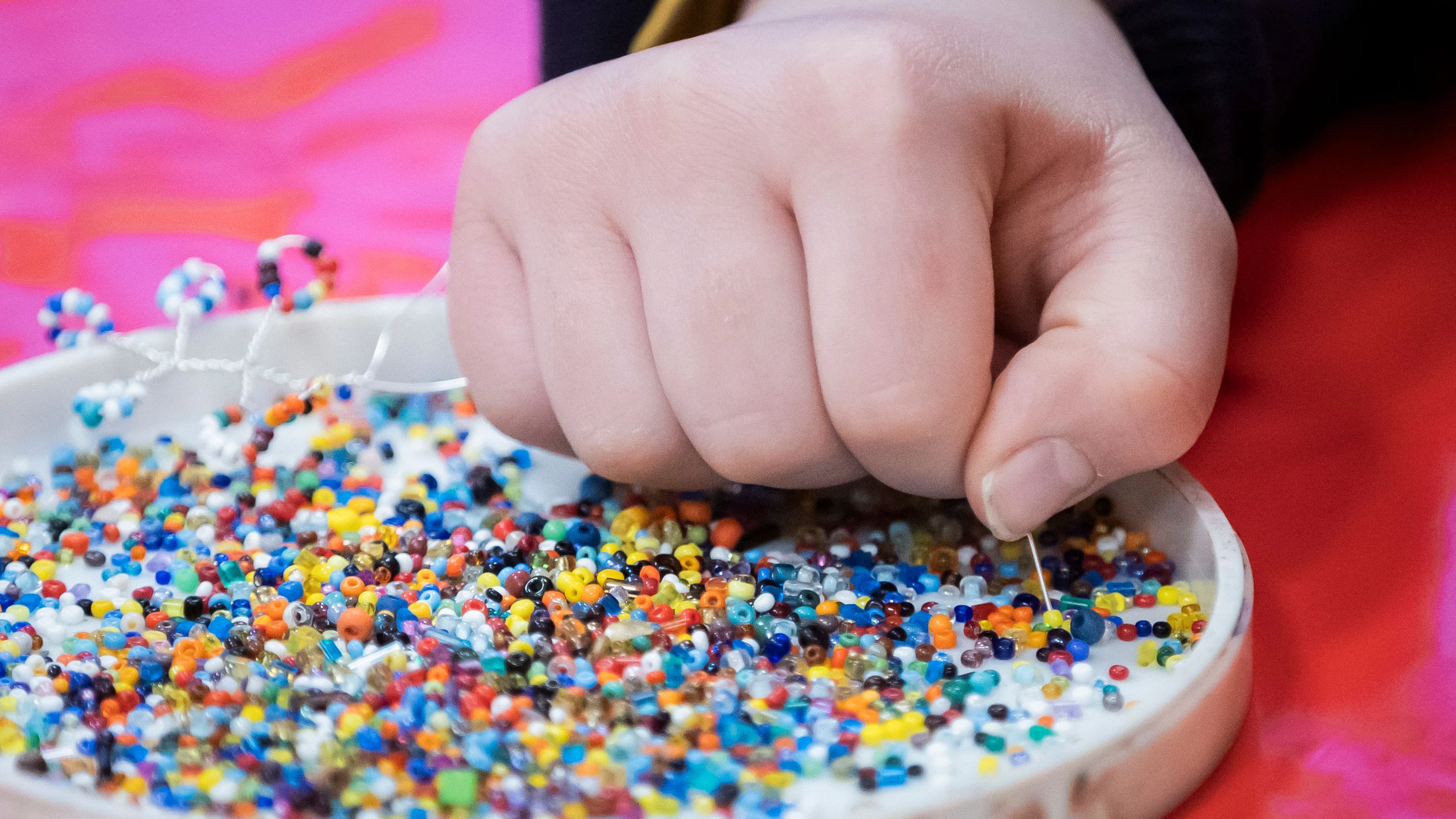 Ein Mädchen fädelt im Kinderklubhaus Perlen für ein Perlenbäumchen auf.