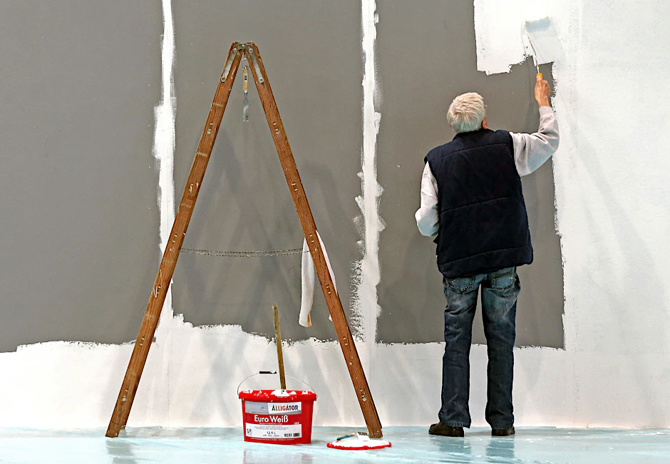 Ein älterer Mann streicht auf der Leipziger Messe eine Wand.&nbsp;