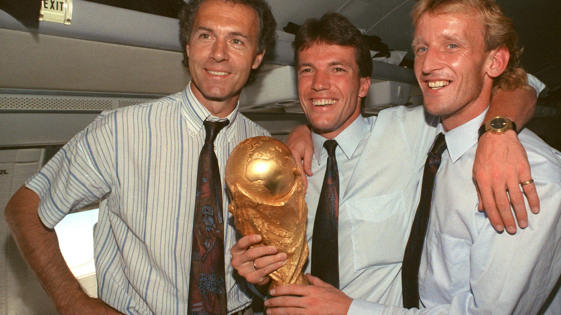1990: Im Flugzeug beim Rückflug von Rom nach Frankfurt präsentieren der damalige DFB-Teamchef Franz Beckenbauer (l), Lothar Matthäus (M) und Andreas Brehme den WM-Pokal.&nbsp;