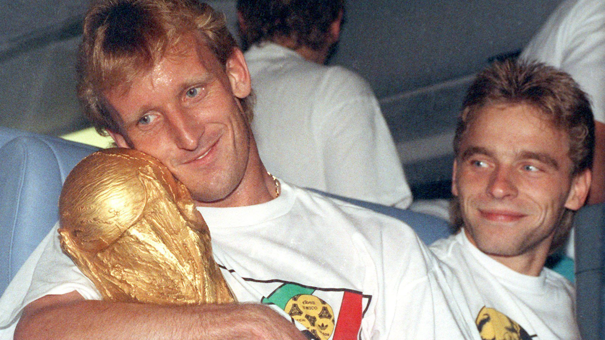 Andreas Brehme (l), kuschelt mit dem WM-Pokal, daneben Teamgefährte Thomas Häßler.
