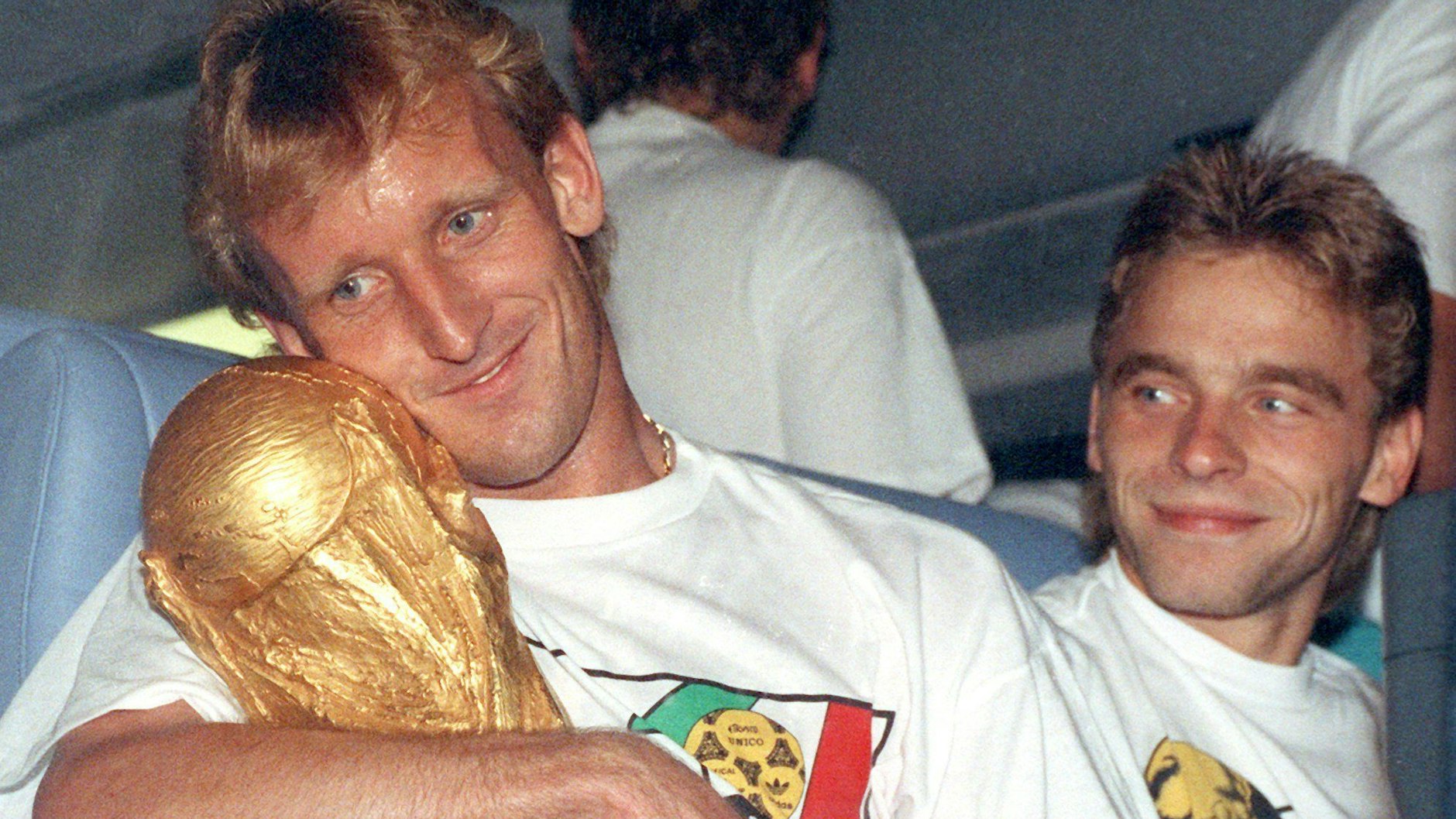 Andreas Brehme (l), kuschelt mit dem WM-Pokal, daneben Teamgefährte Thomas Häßler.
