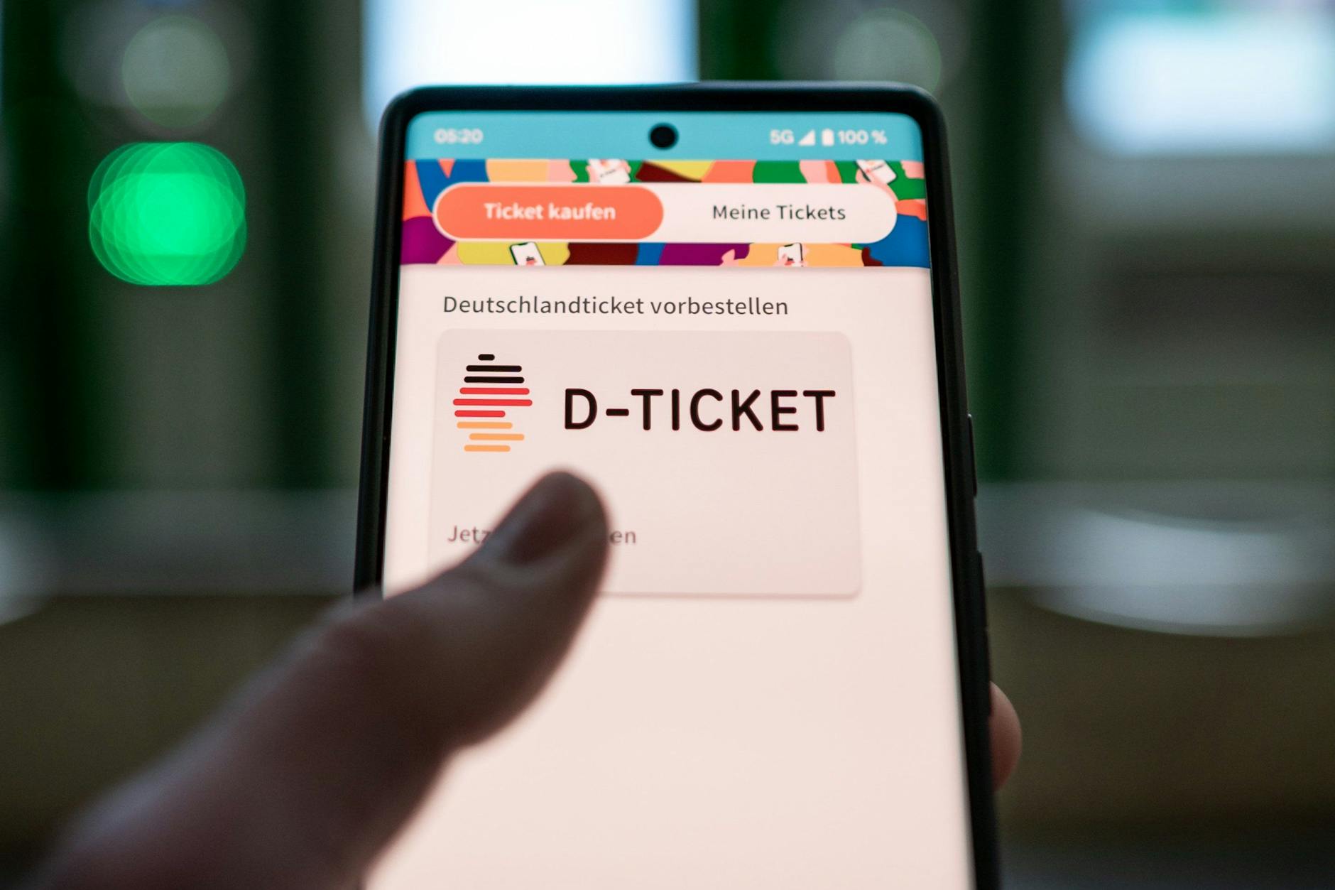 Ein Mann hält ein Mobiltelefon, auf dem das „D-Ticket“ gekauft werden kann, vor Ticketautomaten am Hauptbahnhof in der Hand.