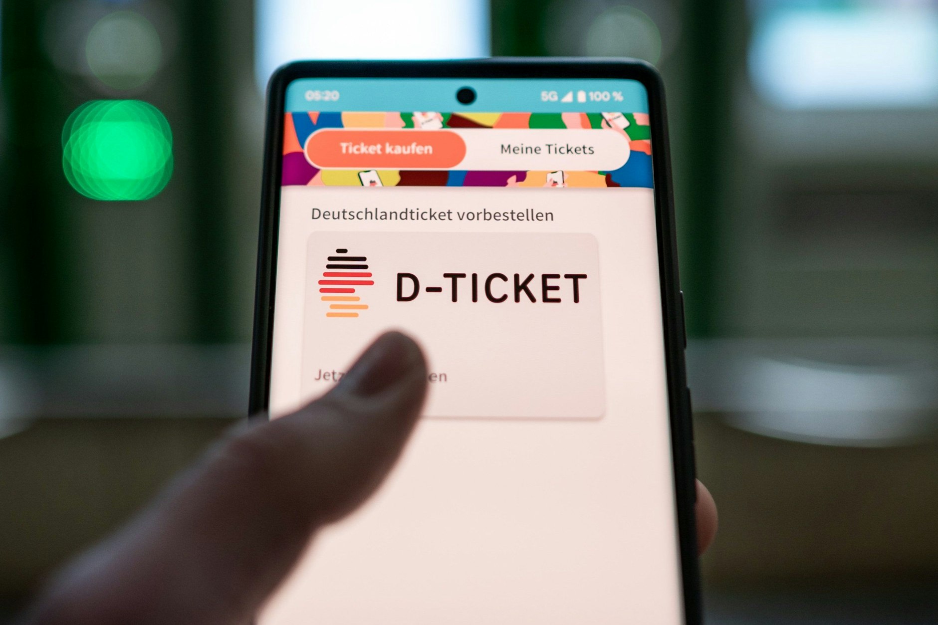 Ein Mann hält ein Mobiltelefon, auf dem das „D-Ticket“ gekauft werden kann, vor Ticketautomaten am Hauptbahnhof in der Hand.