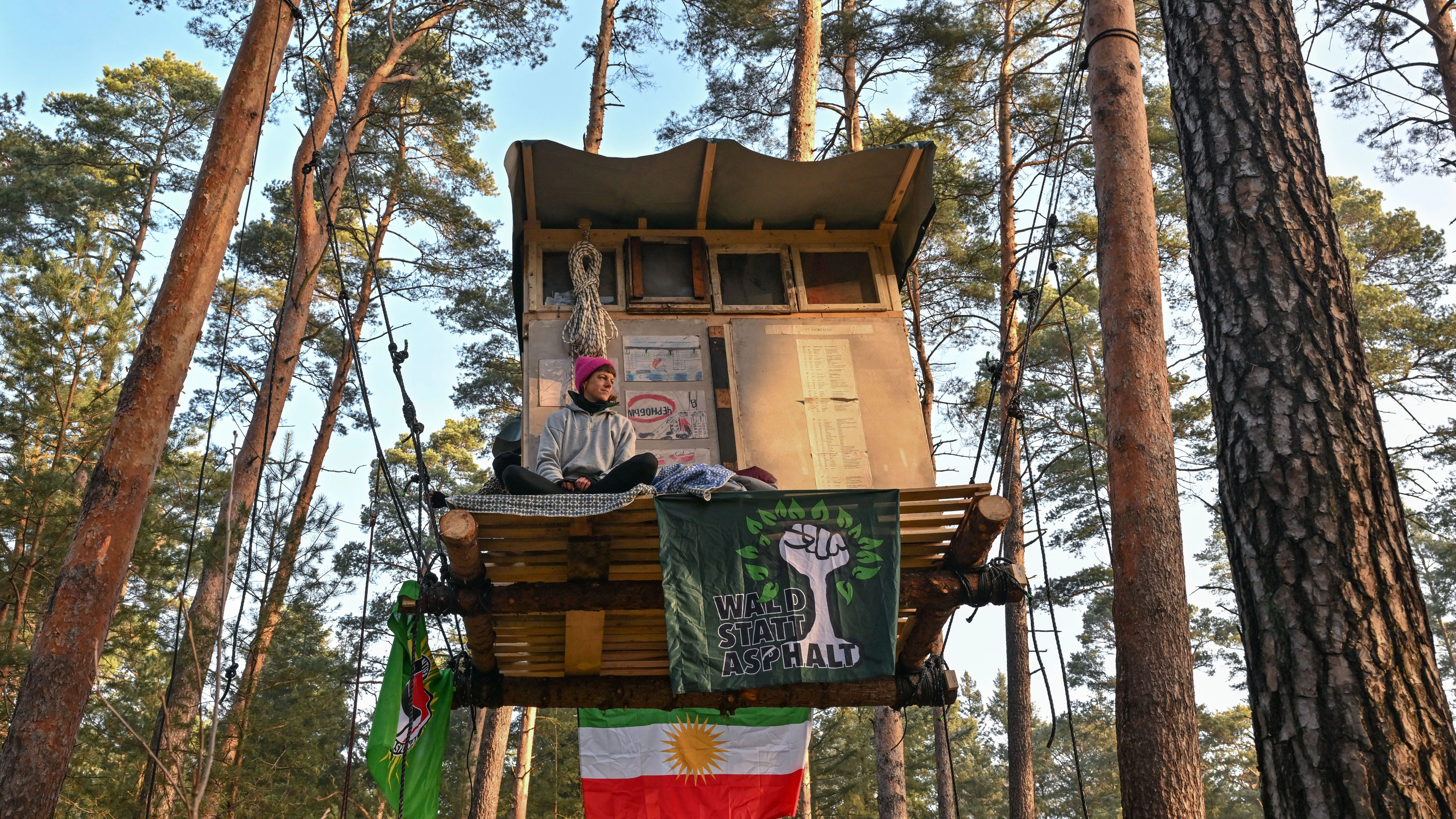 Eine Aktivistin der Initiative „Tesla stoppen“ sitzt auf einem Baumhaus in einem Kiefernwald nahe dem E-Auto-Werk.