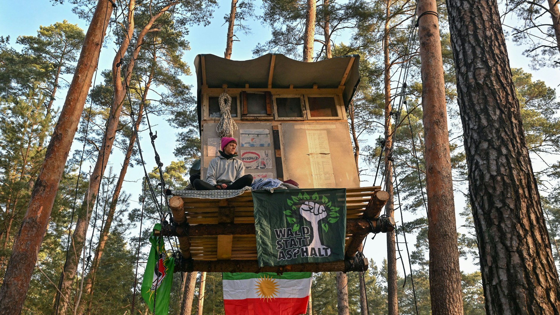 Eine Aktivistin der Initiative „Tesla stoppen“ sitzt auf einem Baumhaus in einem Kiefernwald nahe dem E-Auto-Werk.