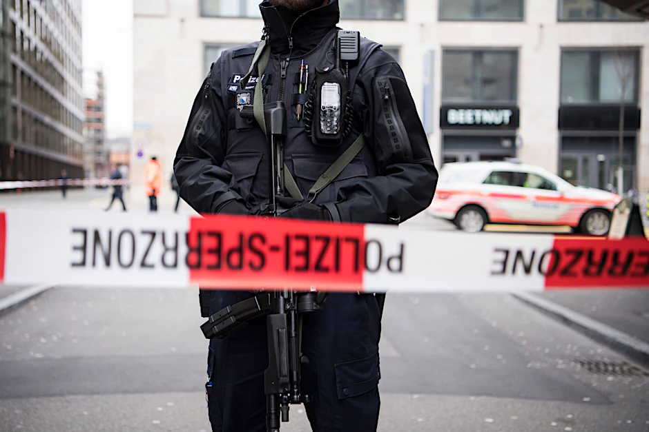 Ein schwer bewaffneter Polizist steht hinter einem Absperrband in der Züricher Innenstadt. 