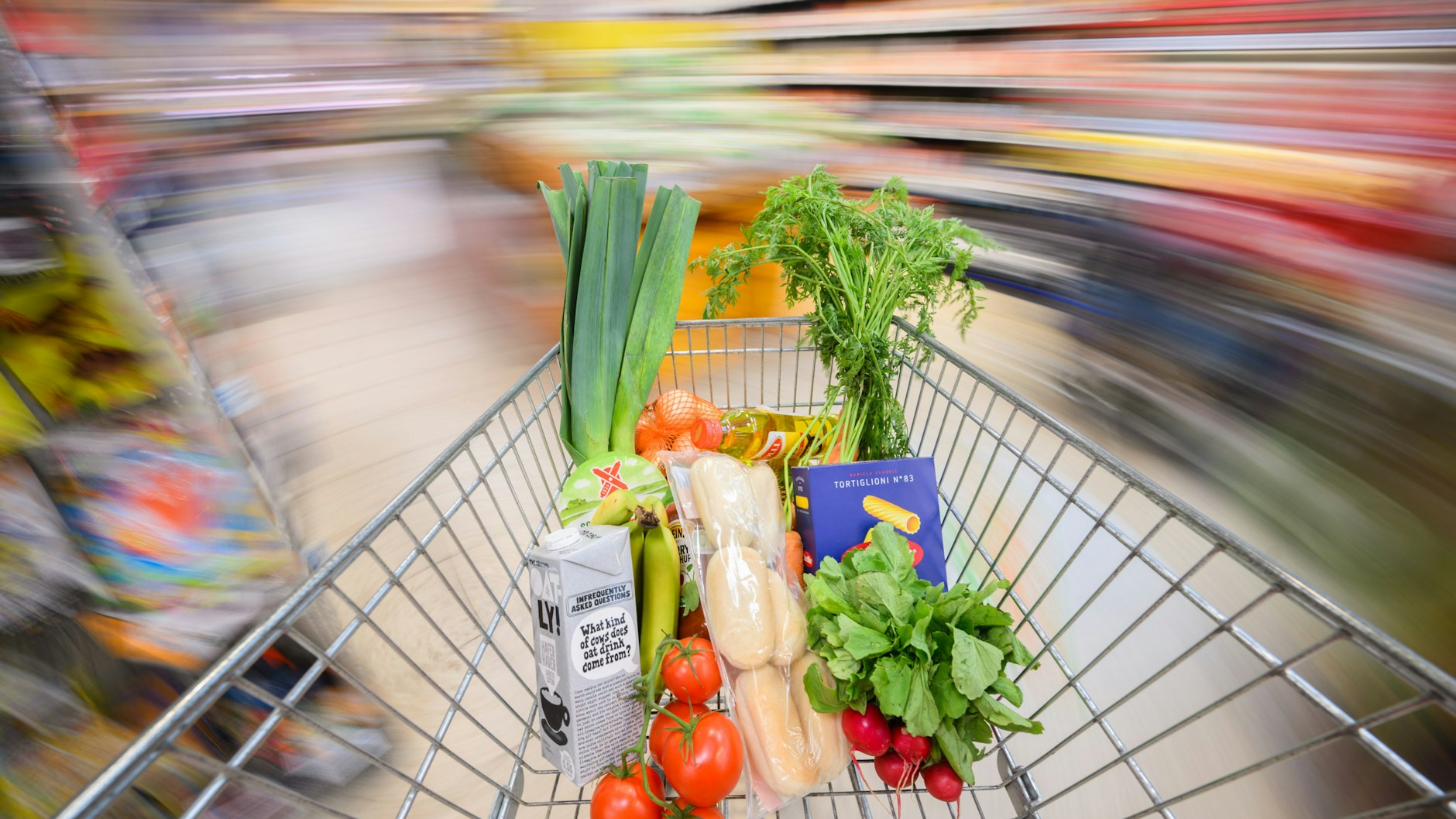 Ein mit Lebensmittel gefüllter Einkaufswagen wird durch einen Supermarkt geschoben.