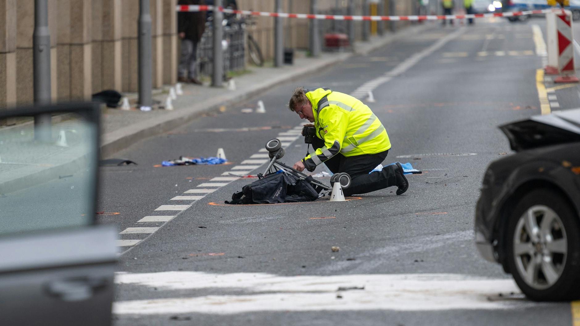 Ein Polizist kniet an einer Unfallstelle in der Leipziger Straße an einem Kinderwagen.