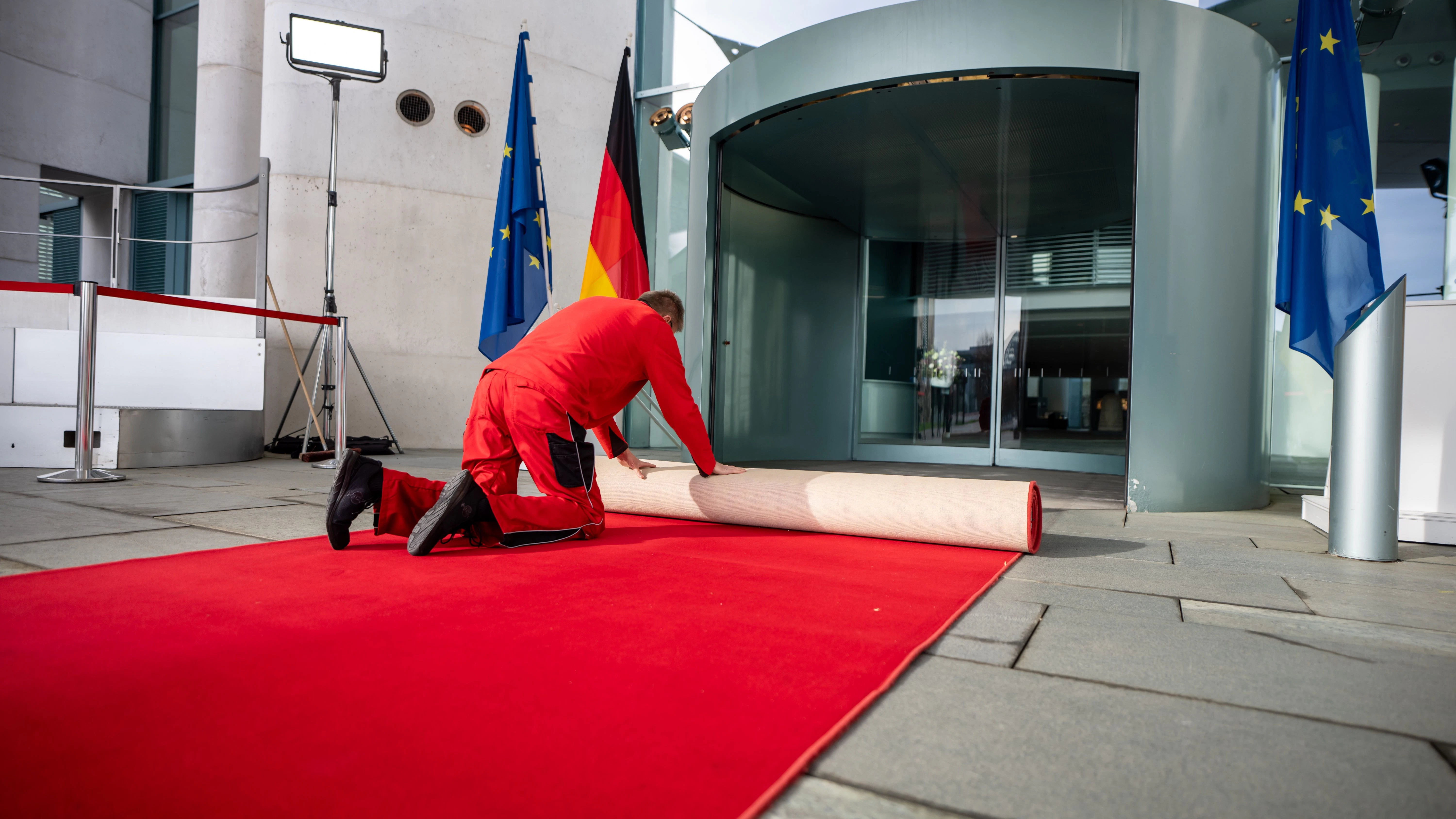 Ein Arbeiter rollt vor dem Treffen von Bundeskanzler Scholz mit Frankreichs Präsident Macron und Polens Regierungschef Tusk den roten Teppich vor dem Kanzleramt aus.