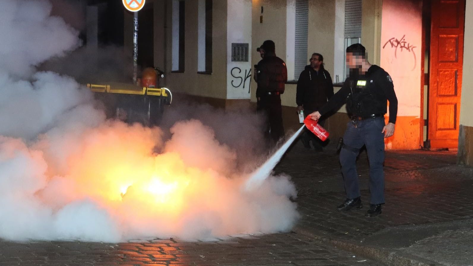 Polizisten versuchten, die brennenden Mülltonnen in der Erlanger Straße in Neukölln zu löschen.