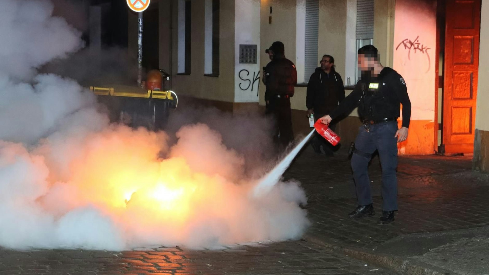 Polizisten versuchten, die brennenden Mülltonnen in der Erlanger Straße in Neukölln zu löschen.