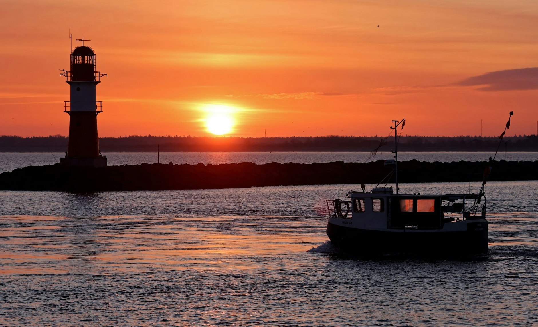 Ein Fischerboot vor der aufgehenden Sonne an der Mole vor Warnemünde: Die bevorstehenden Ostertage versprechen sonniges und relativ mildes Wetter.  