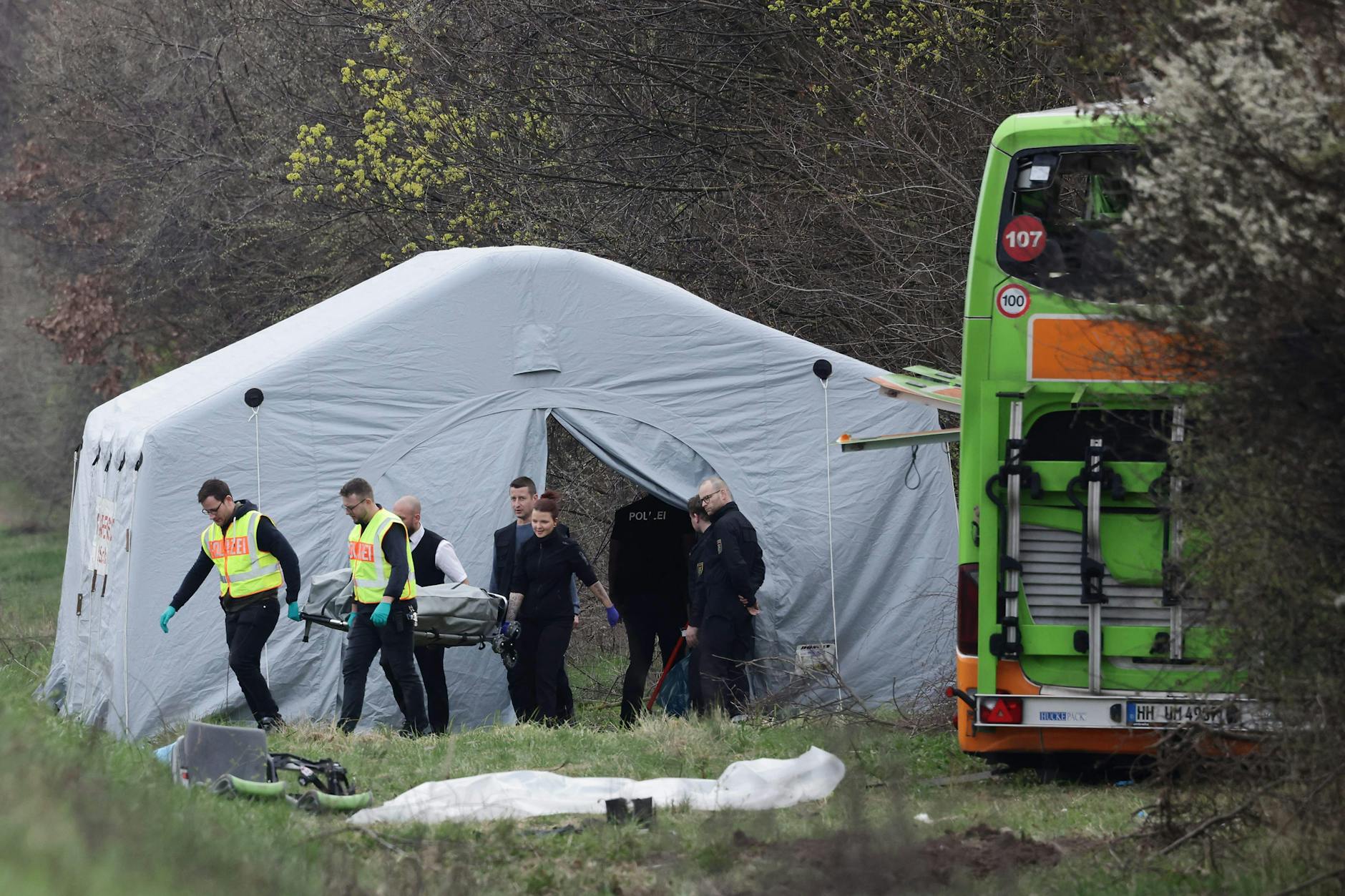 Eine Tote wird in einem Sarg aus einem Zelt neben dem Unglücksbus getragen.