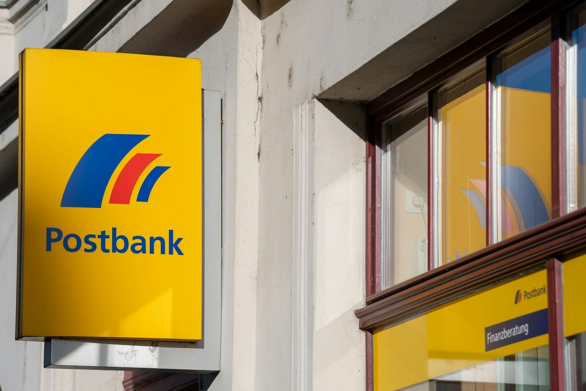 Ein Schild mit dem Logo der Postbank ist an der Fassade einer Bankfiliale angebracht.
