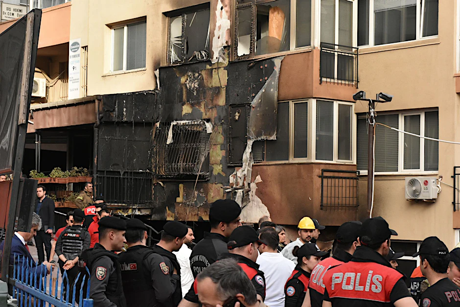 Einsatzkräfte stehen nach einem Brandausbruch vor einem teilweise verbrannten Gebäude.  