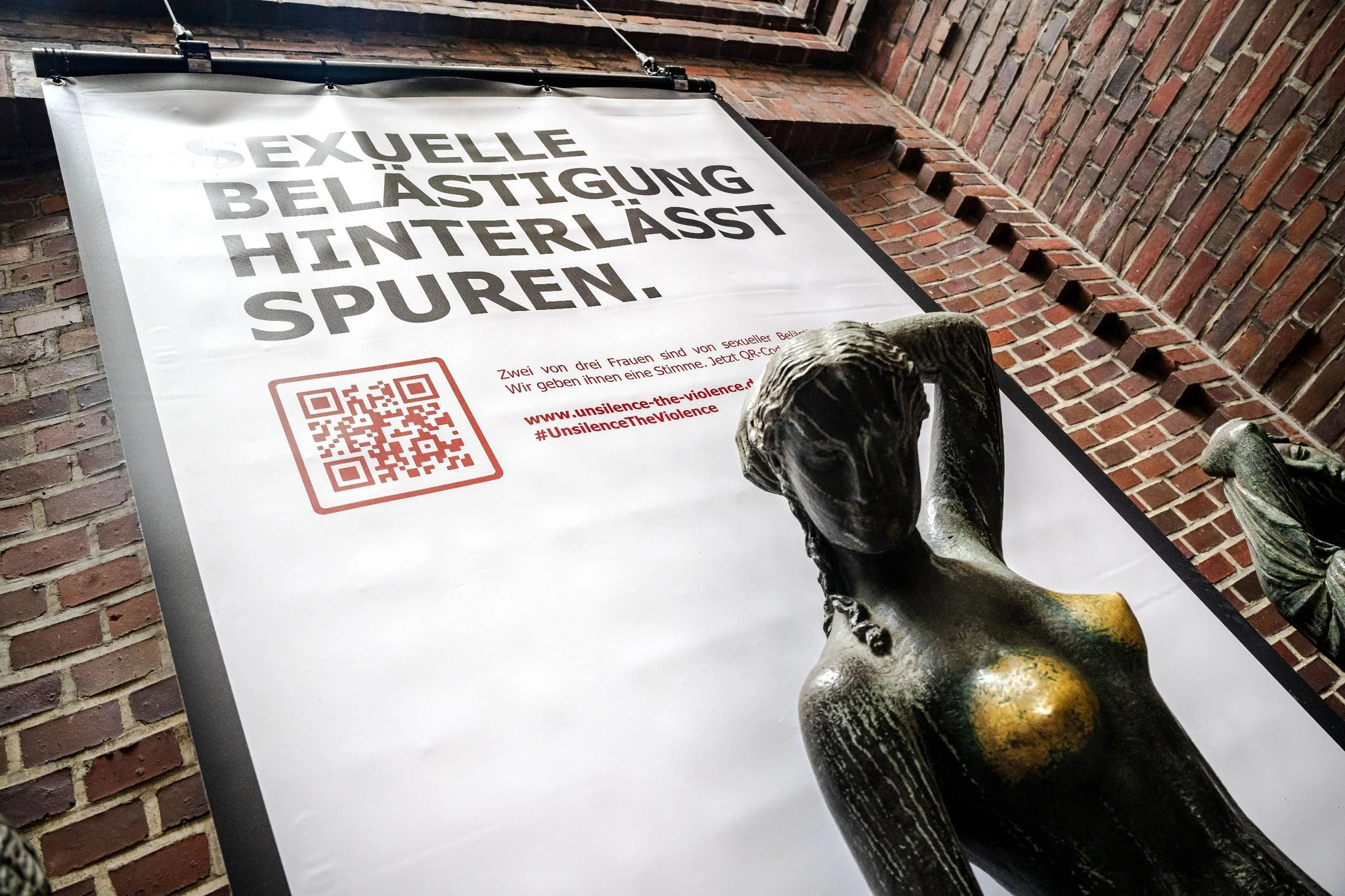 Plakat mit der Aufschrift «Sexuelle Belästigung hinterlässt Spuren» hinter der Bronzeskulptur «Jugend» von Bernhard Hoetger in Bremen.  