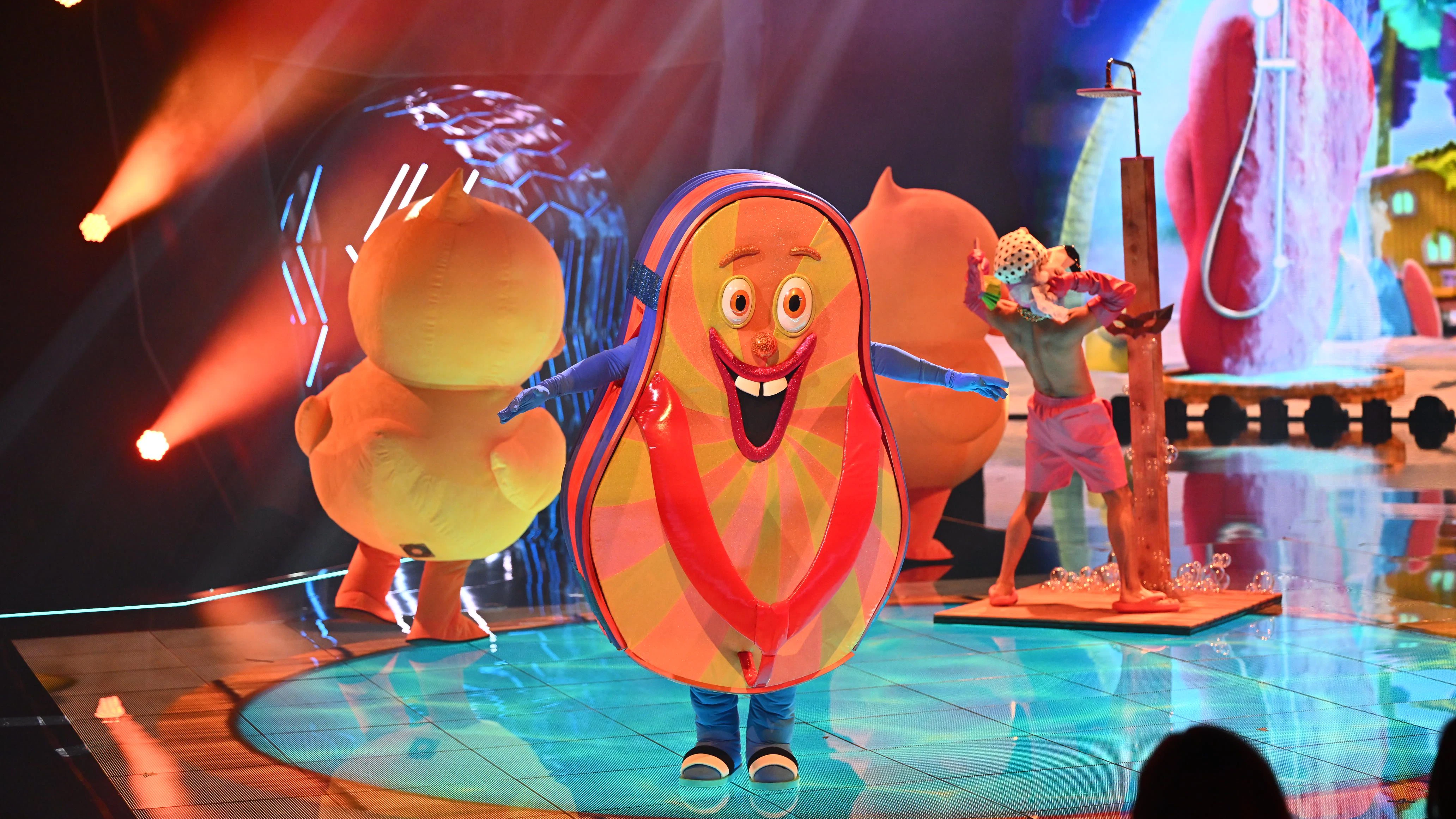 Der Flip Flop in der zweiten Ausgabe von Masked Singer. Die Kleidung unter dem Kostüm ist blau, ein anderes Gesicht zeigt nach vorn.