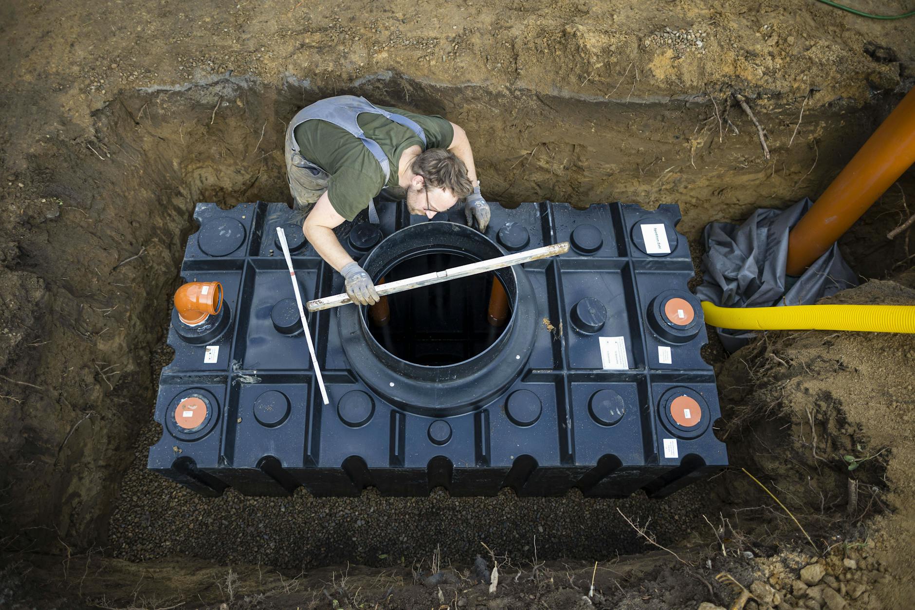 Ein Mann verbaut im Garten neben seinem Haus eine Wasserzisterne. 