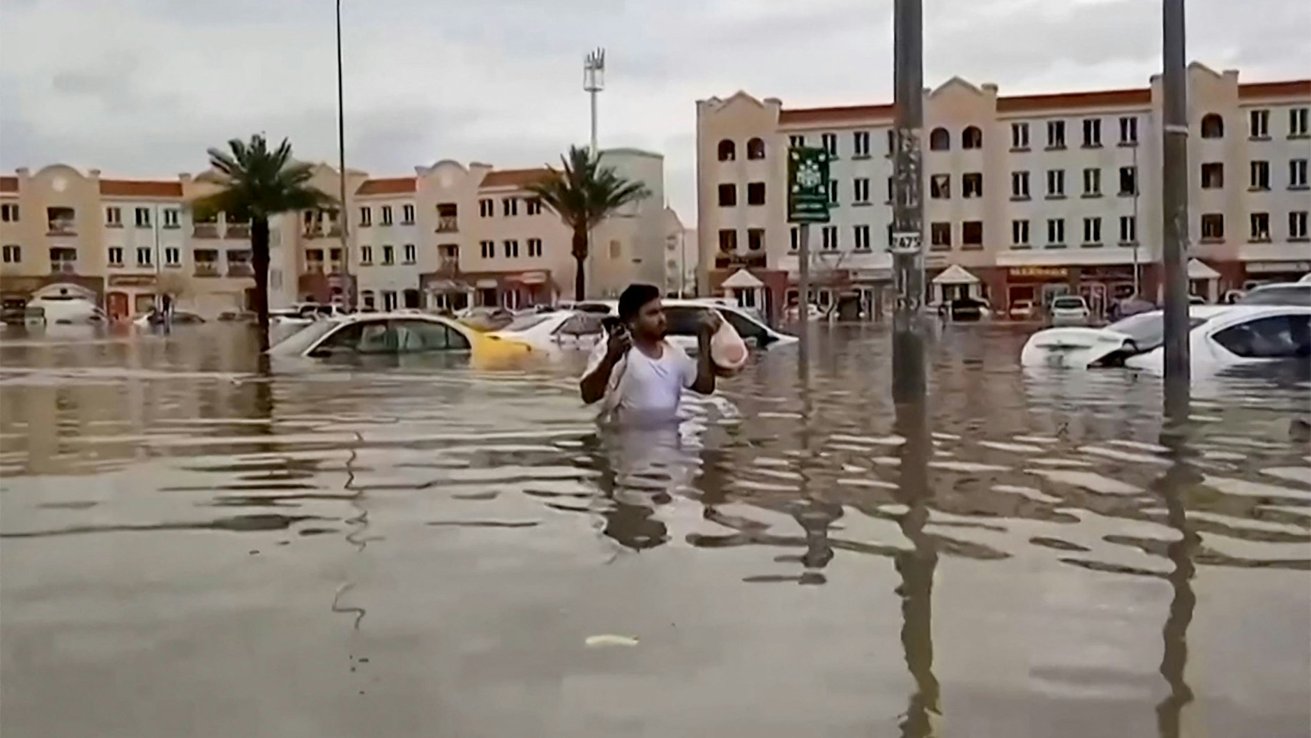 Ein Mann watet im hüfthohen Wasser durch eine überflutete Straße in Dubai.&nbsp;