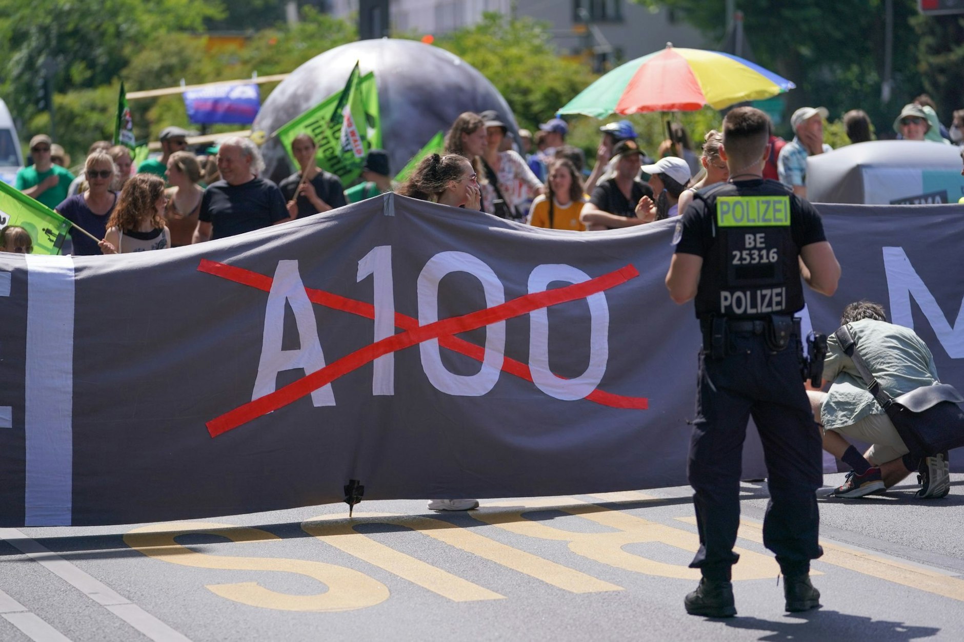 Ein&nbsp;Polizist steht bei einer Demo gegen den Weiterbau der Stadtautobahn A100 vor einem Banner der&nbsp;Demonstranten. Am Sonntag will ein Bündnis erneut demonstrieren.