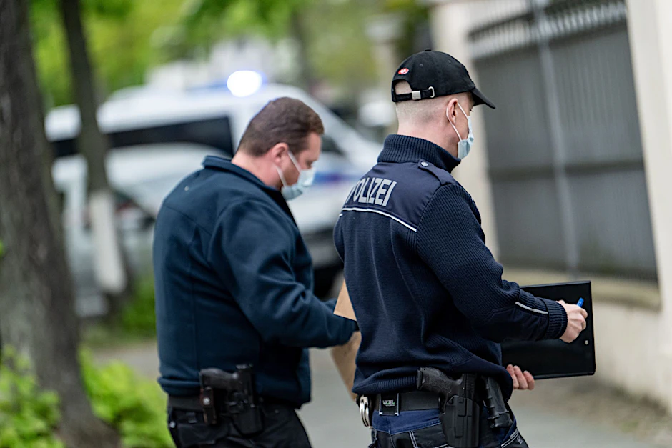 Beamten der Berliner Polizei stehen vor einem Haus an der Königsallee.  