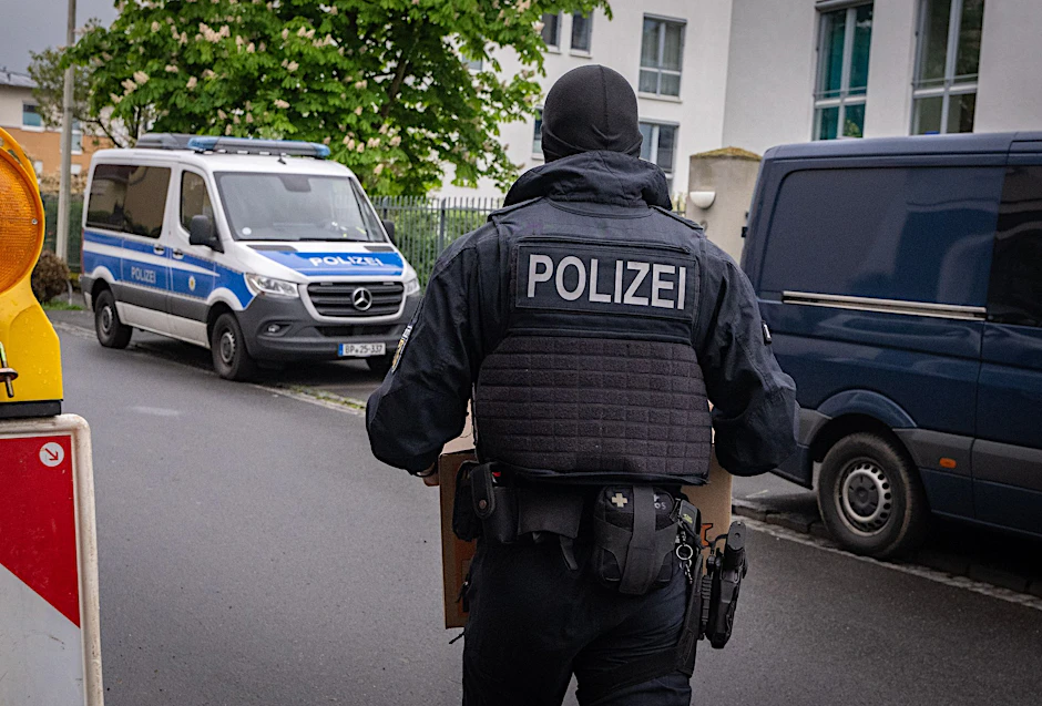 Ein Polizist trägt bei einem Einsatz in Bonn einen Karton mit beschlagnahmtem Material aus einem Gebäude.  