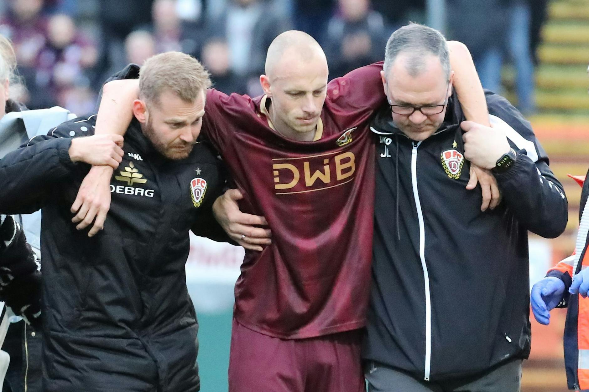 Steffen Eder wird nach dem Unglück von Dynamo-Physio Nils Vielrose (l.) und BFC-Teammanager Jörn Lenz (r.) noch benommen vom Platz geführt.