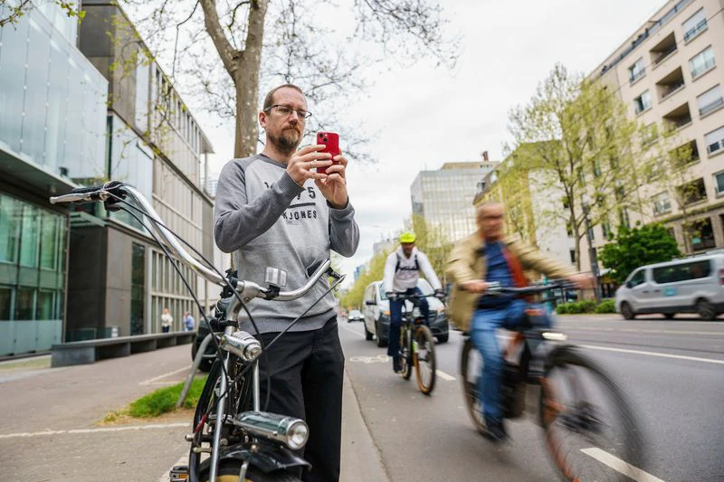 Falko Görres steht auf der Mainzer Landstraße und fotografiert für eine Anzeige ein Lieferservicefahrzeug, das auf dem Radweg parkt.