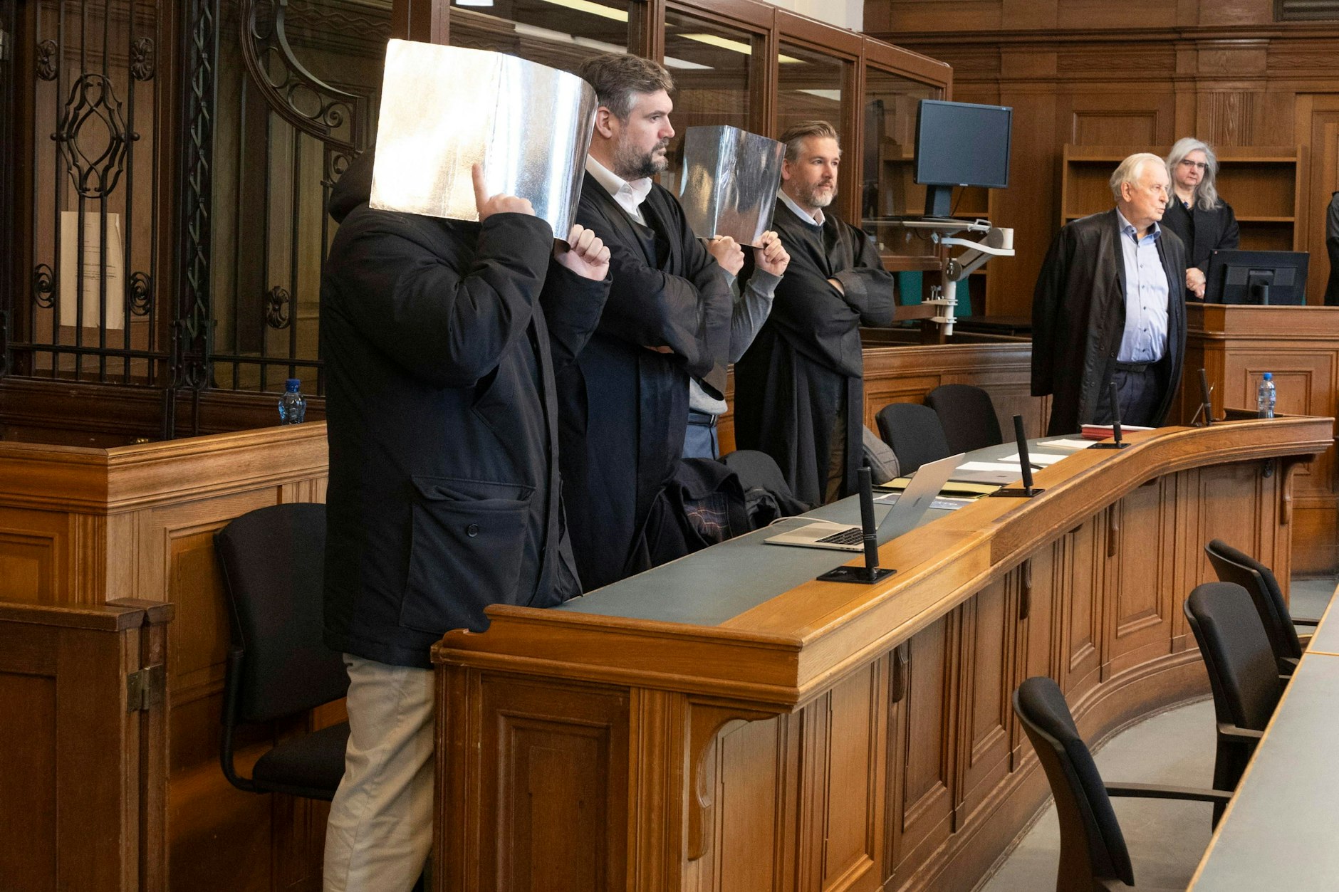 Zwei der mutmaßlichen Vergewaltiger sind auf diesem Foto vom Prozess zu sehen und verstecken sich hinter Aktendeckeln. Neben ihnen stehen ihre Anwälte.