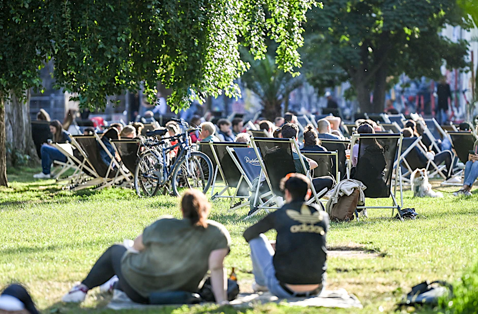 Zahlreiche Menschen sitzen auf Liegestühlen und auf der Wiese in der untergehenden Sonne am Sonntagabend im James-Simon-Park. Am Wochenende kann es in Berlin bis zu 26 Grad warm werden.