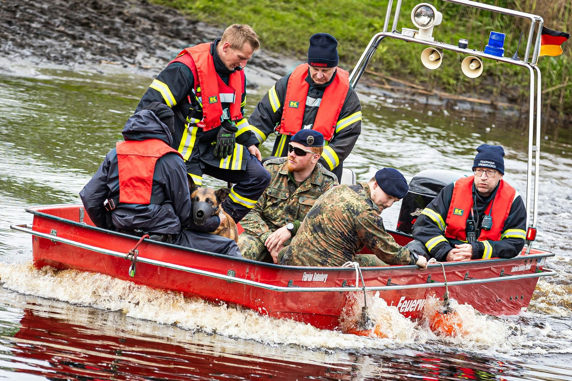 Einsatzkräfte der Feuerwehr und Soldaten der Bundeswehr sind mit einem Suchhund in einem Boot auf dem Fluss Oste unterwegs.