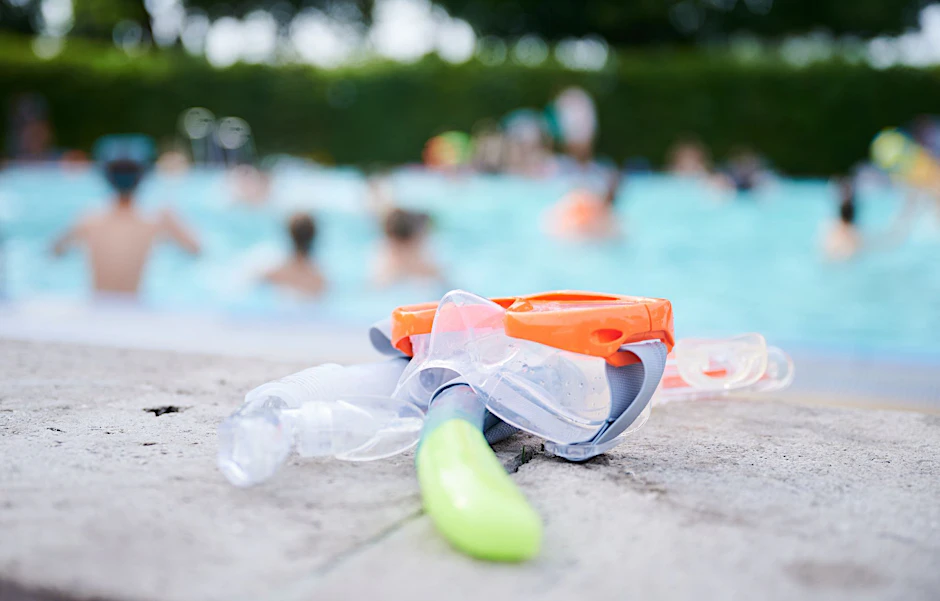 Eine Taucherbrille und Schnorchel liegen in einem Schwimmbad am Beckenrand.  