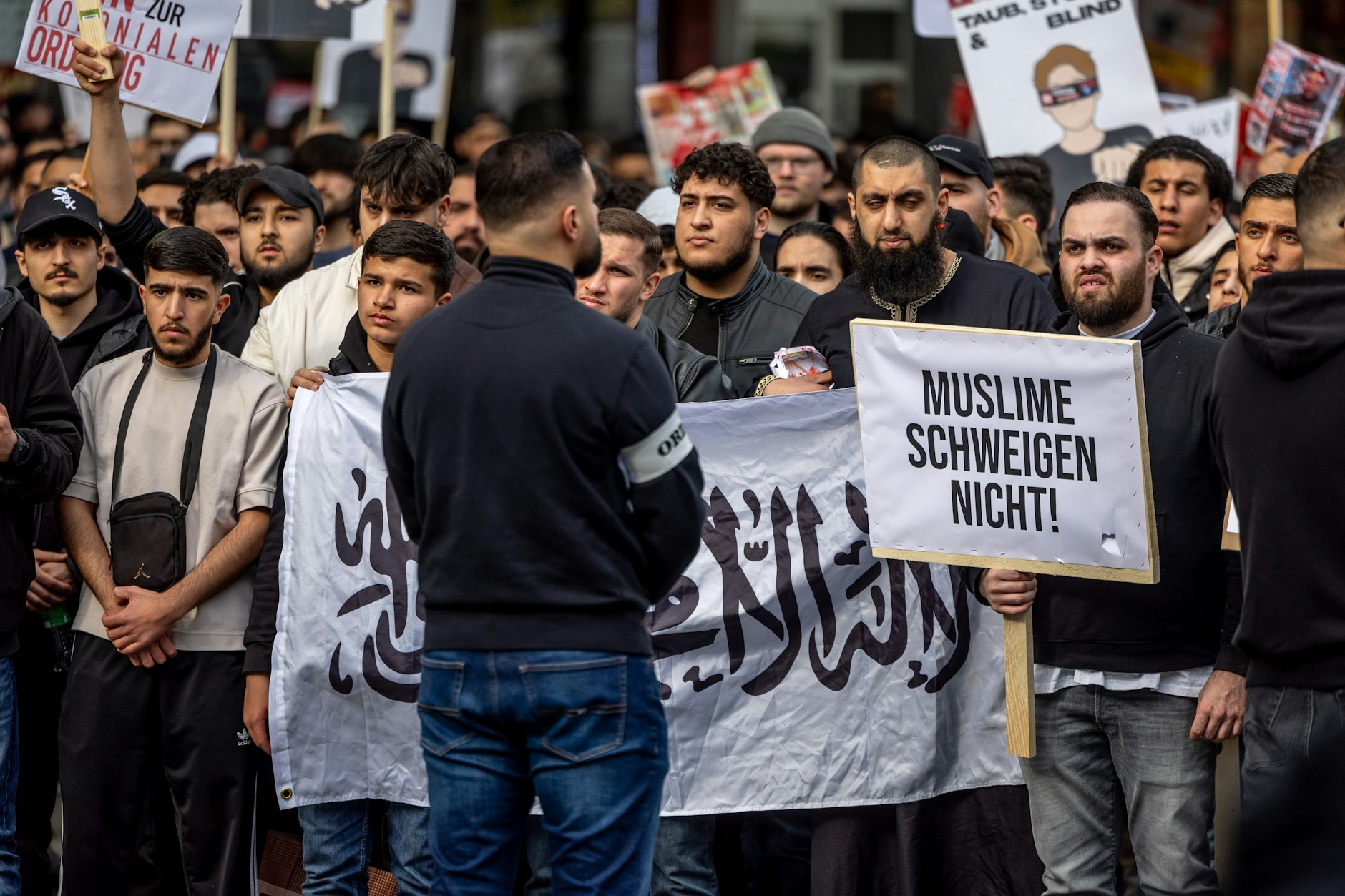 Teilnehmer einer Islamisten-Demo halten ein Plakat mit der Aufschrift „Muslime schweigen nicht“ in die Höhe.