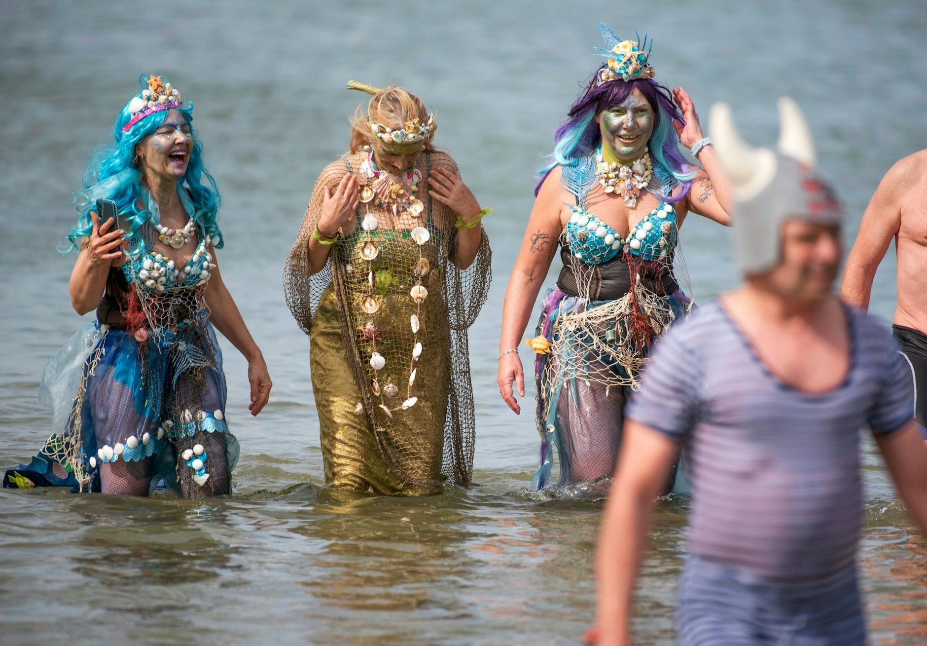 Drei Wassernixen waten aus der acht Grad kalten Ostsee vor Warnemünde: Mit einem letzten Bad, dem Abbaden im Kostüm läuten sie das Ende der Eisbadsaison ein.