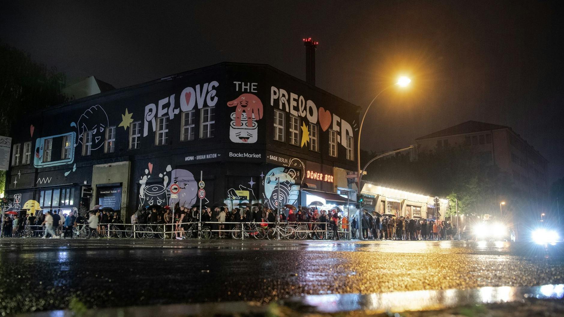 Menschen stehen im strömenden Regen dicht an dicht am Eingang zum Kit Kat Club. 