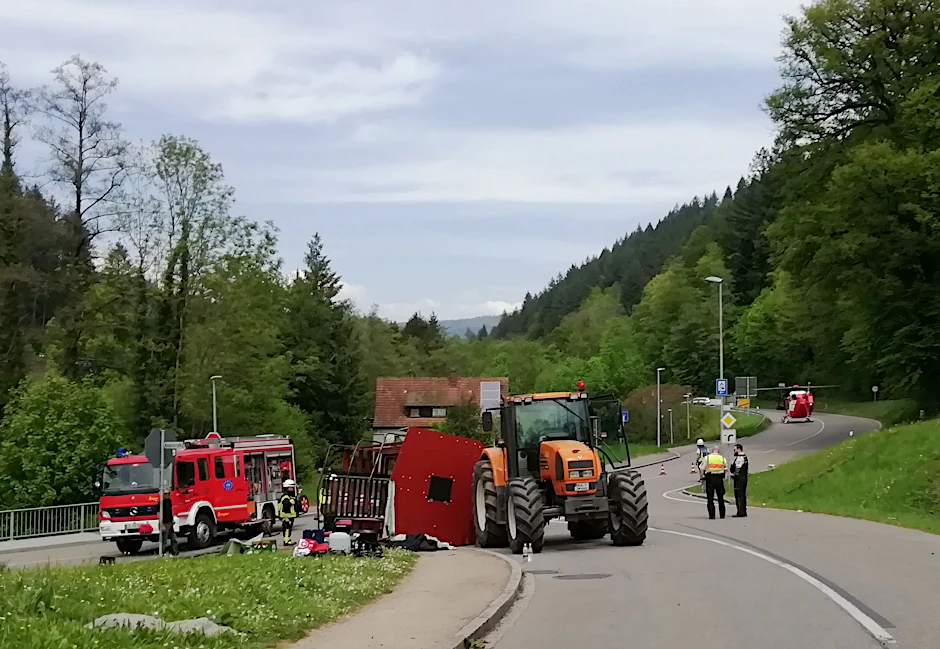 Rettungskräfte stehen nach dem Unfall neben dem umgestürzten Maiwagen, im Hintergrund ein Rettungshubschrauber.