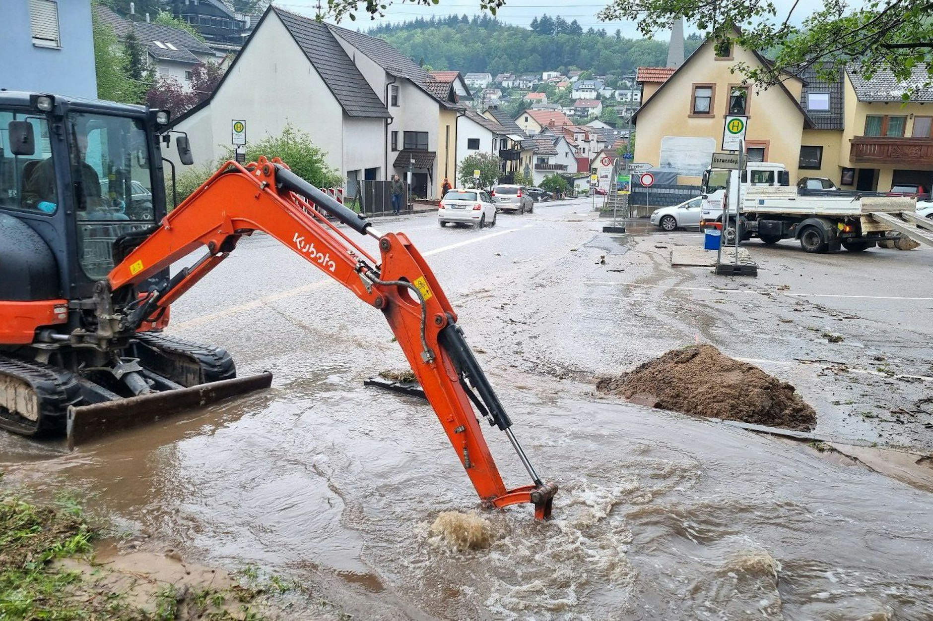 Schriesheim: Mit einem kleinen Bagger wird versucht, den Bestbach freizuschaufeln, um das Wasser von der überfluteten Straße abfließen zu lassen.