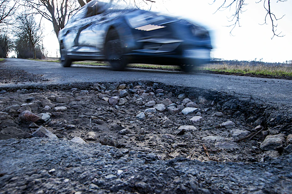 Ein Auto fährt an einem Schlagloch in einer Allee vorbei.
