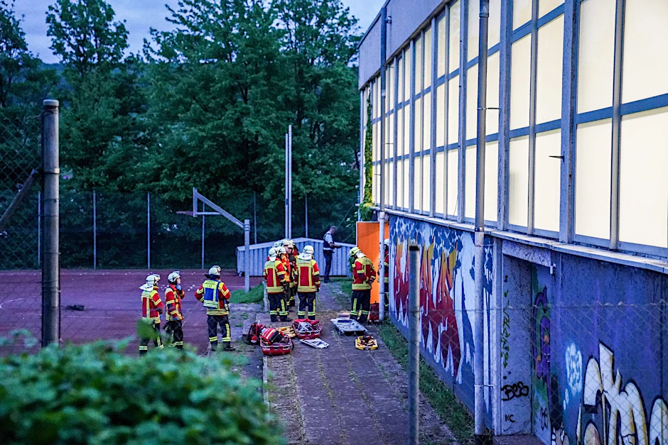 Rettungskräfte stehen vor einer Turnhalle. Vier Kinder sind durch das Dach einer Sporthalle gefallen.  