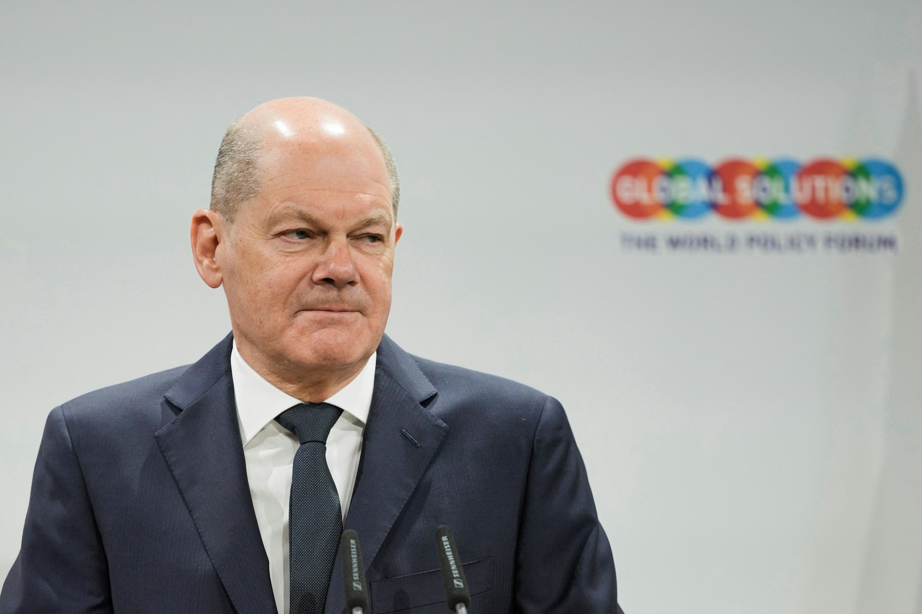 Wollen wir mal davon ausgehen, dass <strong>Olaf Scholz</strong> am Dienstagmorgen völlig arglos in seinen Schrank gegriffen, von 20 Anzügen den erstbesten herausgenommen und sich bei vier Handvoll Exemplaren, die mehr oder minder identisch aussehen, kaum Gedanken gemacht hat, welche nachtblaue Hosen-Sakko-Kombi nun besonders gut zum Global Solutions Summit passt. Dass sein Jäckchen nicht sonderlich gut sitzt und im Schulterbereich wie an den Armen unschön beult? Sei’s drum! Wir finden unter dem Gesichtspunkt der vestimentären Symbolik eher die Kragenverarbeitung fraglich: Zu einer Konferenz, bei der es um die ganz großen geopolitischen Zusammenhänge und mithin auch um Deutschlands Stand in der Welt geht, ausgerechnet ein fallendes Revers? Ein Schelm, wer Böses dabei denkt! Ein enthusiastisch und kraftvoll in die Höhe gerecktes steigendes Revers hätte womöglich ein schöneres Zeichen gesetzt, wenn auch ein ganz kleines …