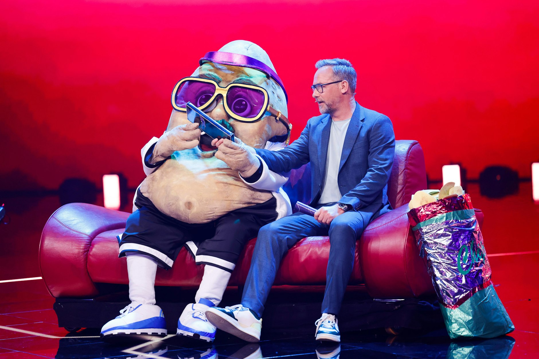 Moderator Matthias Opdenhövel mit der Couch Potato auf der Bühne von The Masked Singer.